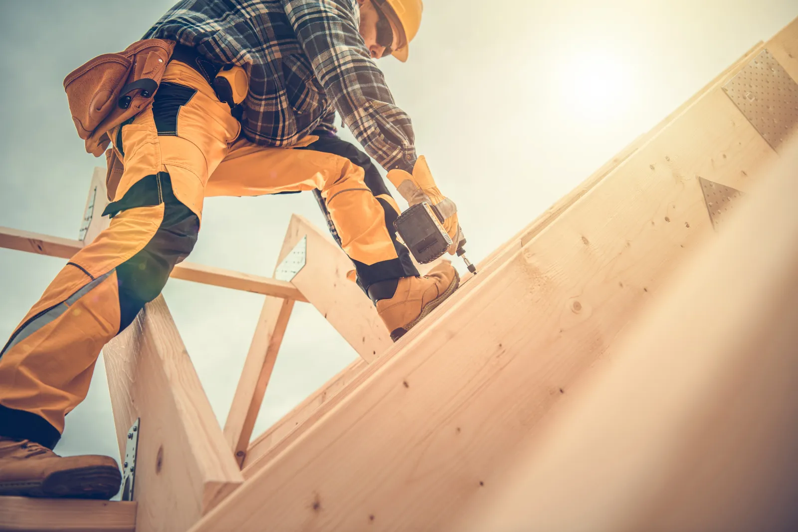 Caucasian Contractor Worker with Drill Driver in His Hand. Carpenter Working on Wooden House Skeleton Frame Roof Section. Construction Industry Theme.