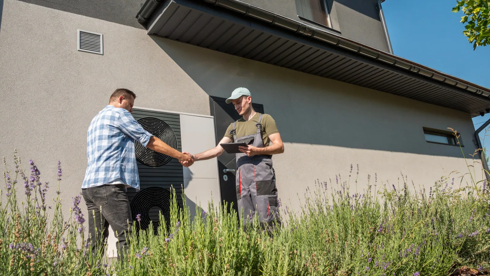A technician and a homeowner discussing heat pump maintenance outside a house, with a heat pump unit visible in the background. High quality photo