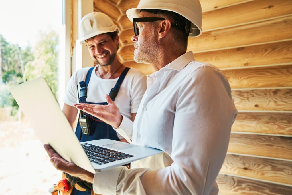 Project manager and contractor discussing on a job site. Project manager is holding a laptop.