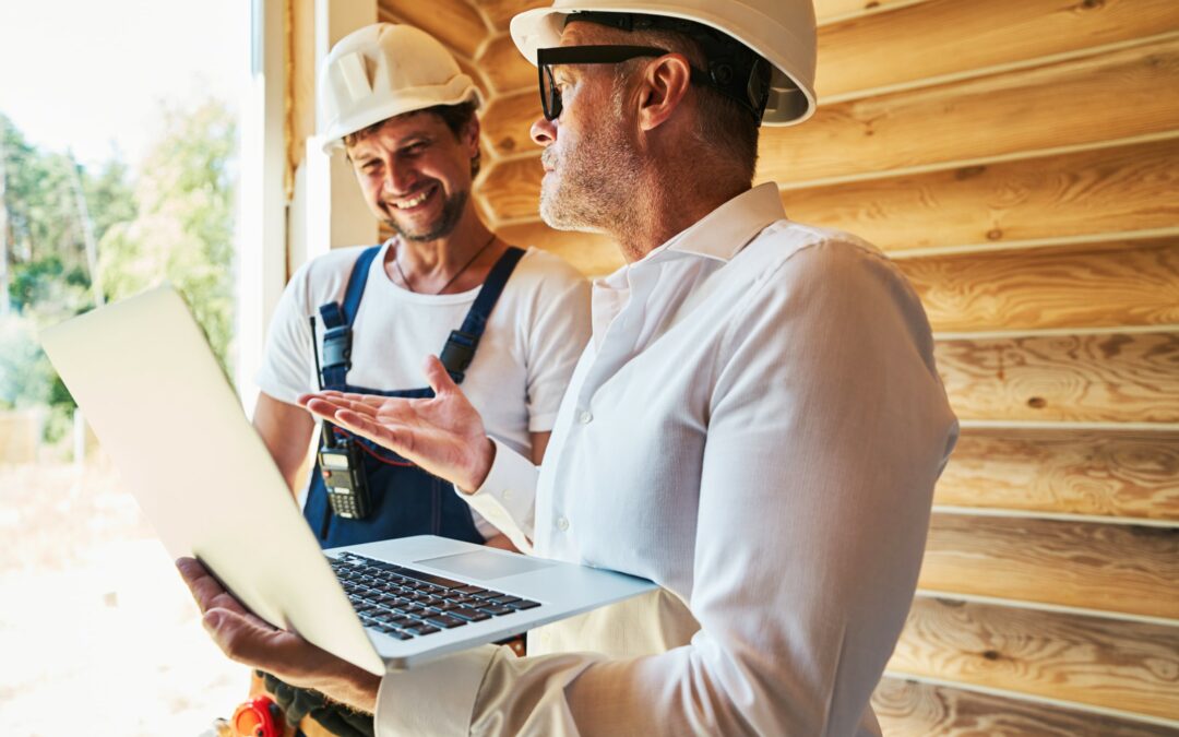 Project manager and contractor discussing on a job site. Project manager is holding a laptop.