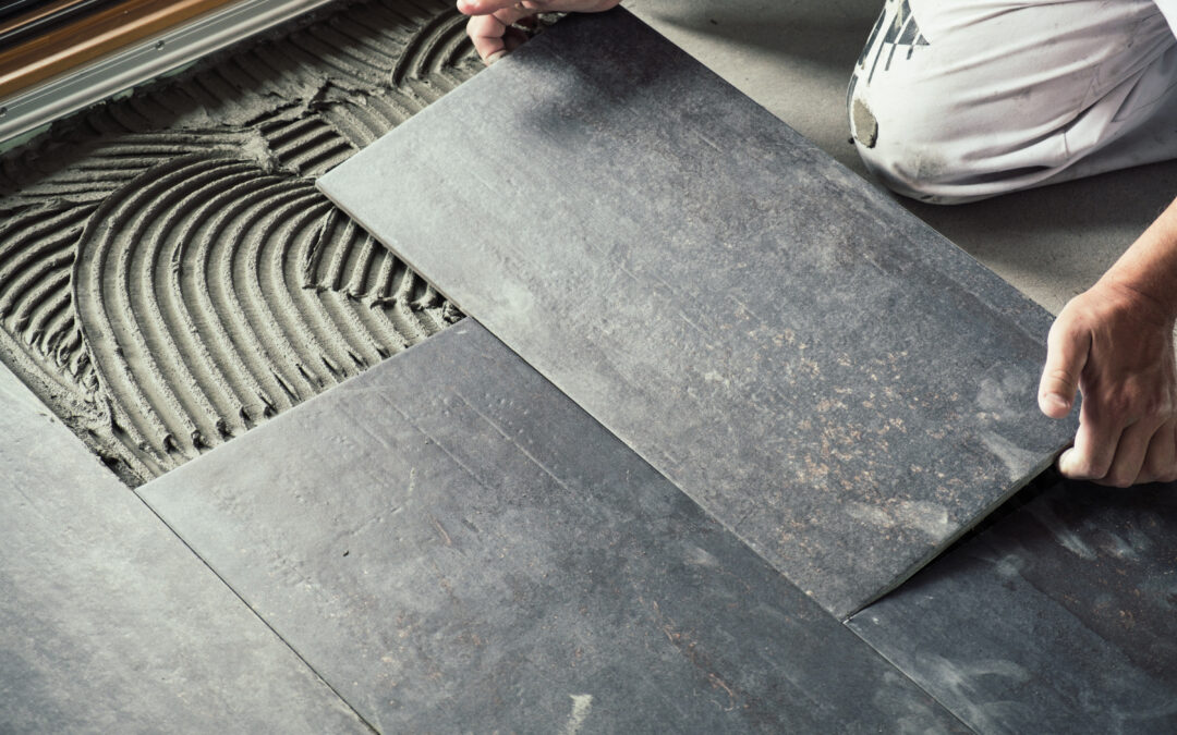 Worker placing dark grey ceramic floor tiles on adhesive surface