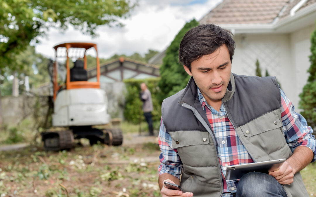 Landscaping contractor outside using tablet, digger in background