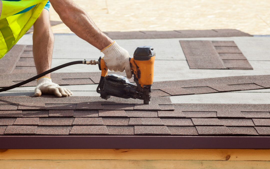 Construction worker putting the asphalt roofing (shingles) with nail gun on a new frame house